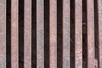 Iron grate over the drainage channel on the road. Rusty texture and scuffs on the metal. Horizontal.