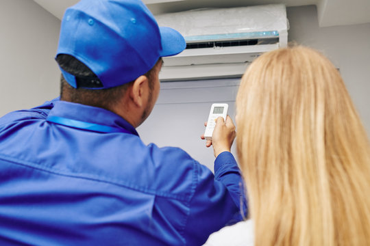 Service worker explaining female customer how use remote control to change temperature with air conditioner