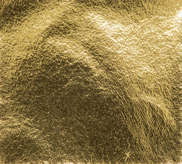 Real gold foil texture background with light reflections.