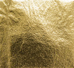 Real gold foil texture background with light reflections.