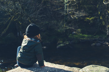Little preschooler sitting on rock by brook