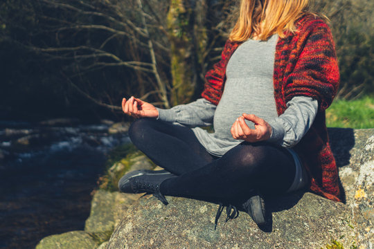 Pregnant woman in meditative pose on rock by brook