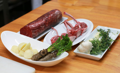 Raw boneless beef, bone rib-eye steak on a plate with onion, garlic and garnish ingredients on a kitchen table.