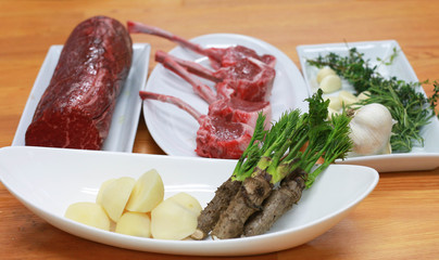 Raw boneless beef, bone rib-eye steak on a plate with onion, garlic and garnish ready to cook. Preparing ingredients on a wooden table.