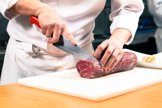 Chef Cutting A Large Raw Boneless Beef Steak Meat On A White Cutting Board.