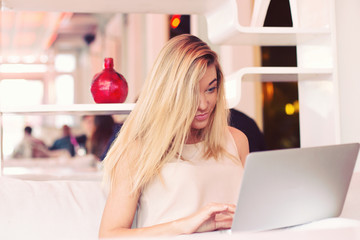 a beautiful blond young businesswoman is working  on a laptop in a cafe early  in the morning