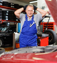 Puzzled male mechanic inspecting broken car and determining scope of work at auto service