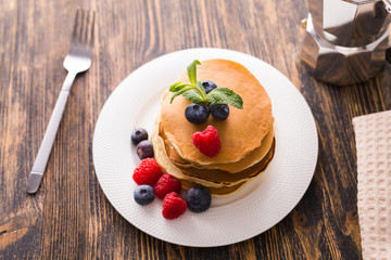 Homemade sweet pancakes with blueberries and raspberries on a white plate, top view.
