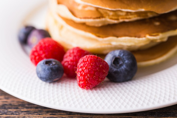 Pancakes with blueberries and raspberry on wooden background. Breakfast and traditional meal.