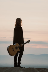 long haired bearded guy with guitar standing in the sunset
