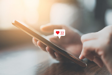 Woman hand using smartphone with heart icon at coffee shop background. Technology business and social lifestyle concept.