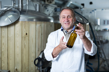 Portrait of brewer who is standing with bottle for beer on his workplace