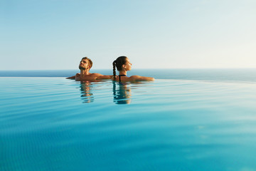 Couple In Love At Luxury Resort On Romantic Summer Vacation. People Relaxing Together In Edge...