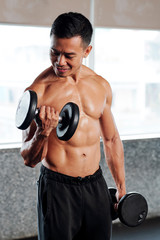 Strong Vietnamese sportsman lifting dumbbells and showing his muscular body