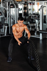Fototapeta na wymiar Strong shirtless Vietnamese man training with battle ropes in gym as part of fat burning workout