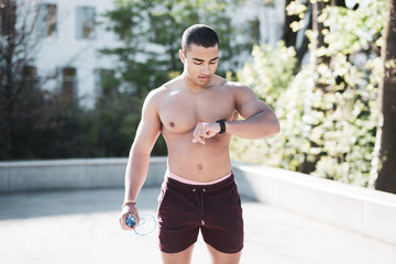 Mann mit freiem Oberk&ouml;rper schaut beim Training auf seinen Fitness-Tracker / Pulsuhr