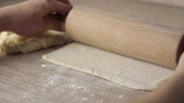 Flattening dough for croissant with roller on wooden table, static