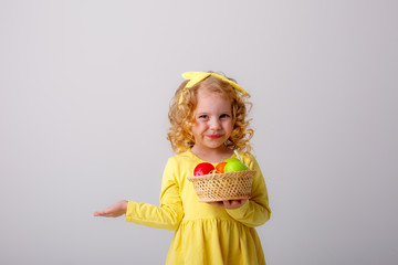 a small curly haired blonde girl smiling holding a basket of Easter eggs on a white background