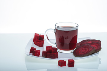 sliced pieces of raw beet and beetroot juice in glass with parsley on plate isolated on white background, close view root