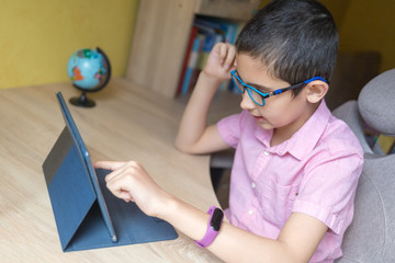 Boy in glasses studying homework with tablet PC during his online lesson. Quarantine. Distance learning. Remote education.