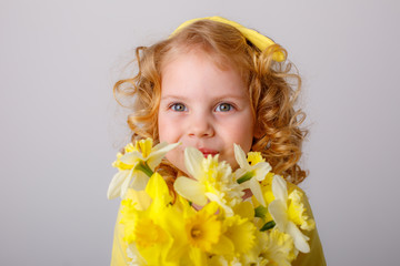 a small curly haired girl in a yellow dress holding a bouquet of spring flowers on a white background smiles