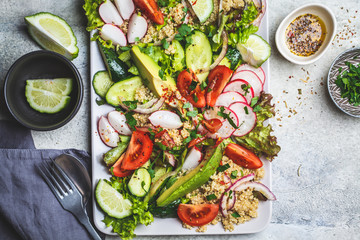 Quinoa salad with tomato, cucumber, radish and avocado on gray plate, top view. Healthy vegan food concept.