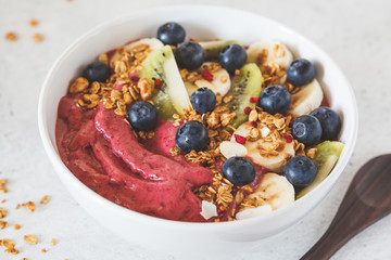 Pink berry smoothie bowl with fruits, berries and granola in white bowl on white background.