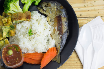 Mackerel with steamed rice in a black plate decoration with broccoli vegetables and carrots.
