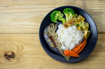 Mackerel with steamed rice in a black plate decoration with broccoli vegetables and carrots.