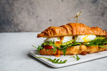 Croissant sandwich with poached egg, tomato and guacamole on white board. Breakfast food concept.