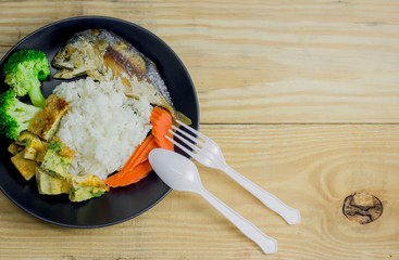 Mackerel with steamed rice in a black plate decoration with broccoli vegetables and carrots.