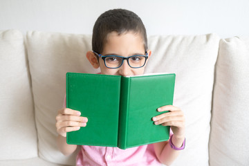 Boy in pink t-shirt sits at home on cozy sofa, reads book. Light background. Quarantine. Holidays.