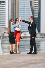 Obraz premium Celebrating success. Two happy young businesswomen giving high five while their man colleague outdoors