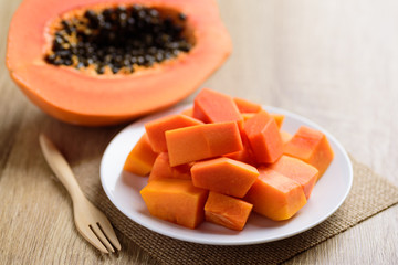 Sliced ripe papaya fruit on white plate with fork ready to eating on wooden background, Tropical...