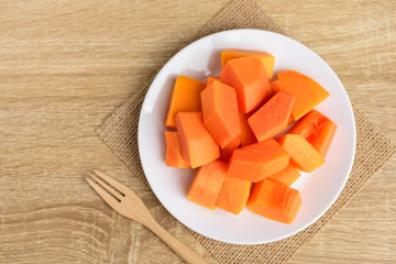Sliced ripe papaya fruit on white plate with fork ready to eating on wooden background, Tropical fruit, Top view
