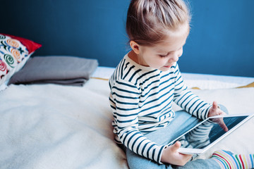 Cute kid watching cartoons at home using wireless tablet computer. Girl toddler growing with gadget in cozy place