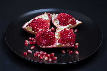 Pomegranate peeled in a black plate on a black background, close-up