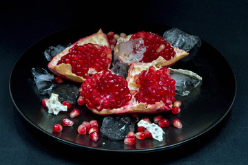 Pomegranate peeled, ice in a black plate on a black background, close-up