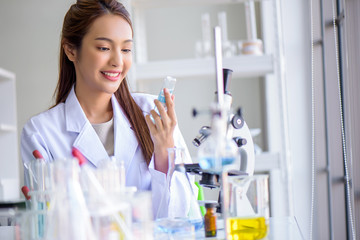 Attractive young Asian scientist woman lab technician assistant analyzing sample in test tube with microscope at laboratory. Medical, pharmaceutical and scientific research and development concept.