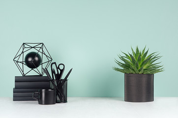 Simple minimalistic office interior with black stationery, books, coffee cup, aloe plant, abstract sculpture in green mint menthe interior on white wood table, copy space.
