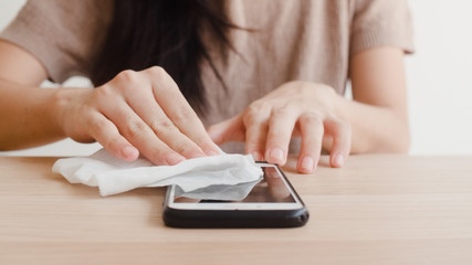 Fototapeta premium Asian woman using alcohol spray on tissue clean mobile phone before use it for protect coronavirus. Female clean surface for hygiene when social distancing stay at home and self quarantine time.