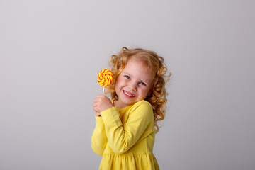 little curly blonde girl smiling holding a Lollipop hiding on a white background