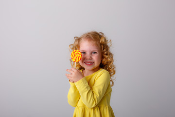 little curly blonde girl smiling holding a Lollipop hiding on a white background