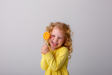 little curly blonde girl smiling holding a Lollipop hiding on a white background