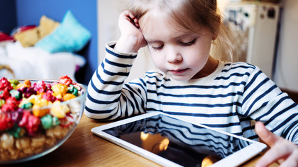 Young girl playing kid's application using wireless tablet computer. Toddler growing with gadget in cozy place