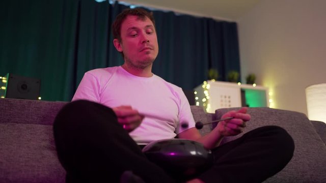 a man sits at home and plays on the hapi drum
