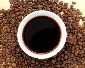 Coffee cup on wooden kitchen table with coffee beans. Top view with morning sunlight