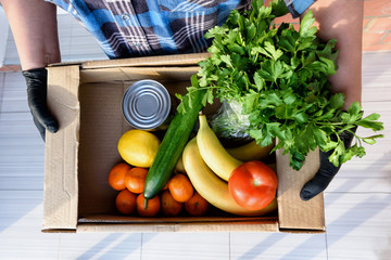 Hands holding the donation box full of groceries, fruits and vegetables. View from top