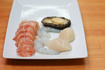 Fresh raw seafood cooking ingredients on a white plate. Peeled lobster, shrimp, prawns and abalone ready to cook.