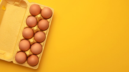 Brown chicken eggs in cardboard box on yellow background, top view